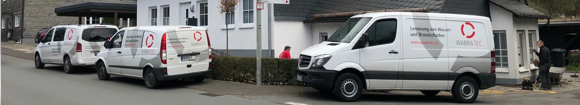 Drei weiße Handwerker-Autos der Firma WABRA TEC stehen vor einem weißen Haus mit schwarzem Dach.