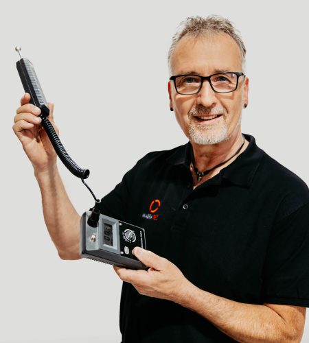 Ein Trocknungstechniker der Firma WABRA TEC hat ein schwarzes T-Shirt mit Firmenlogo an und hält in den Händen ein Gerät zur Feuchtigkeitsmessung.