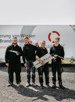 Vier Mitarbeiter mit schwarzer Arbeitskleidung und ihren jeweiligen Arbeitsgeräten in der Hand, repräsentieren die angebotene Leistungen der WABRA TEC GmbH.